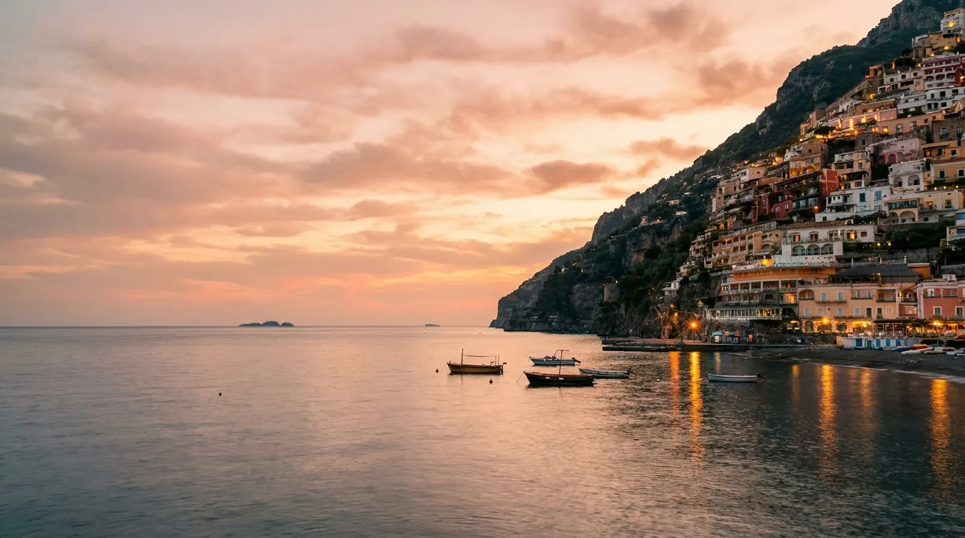 Pastel cliffside Italian coastal village glowing at dusk above a calm sea