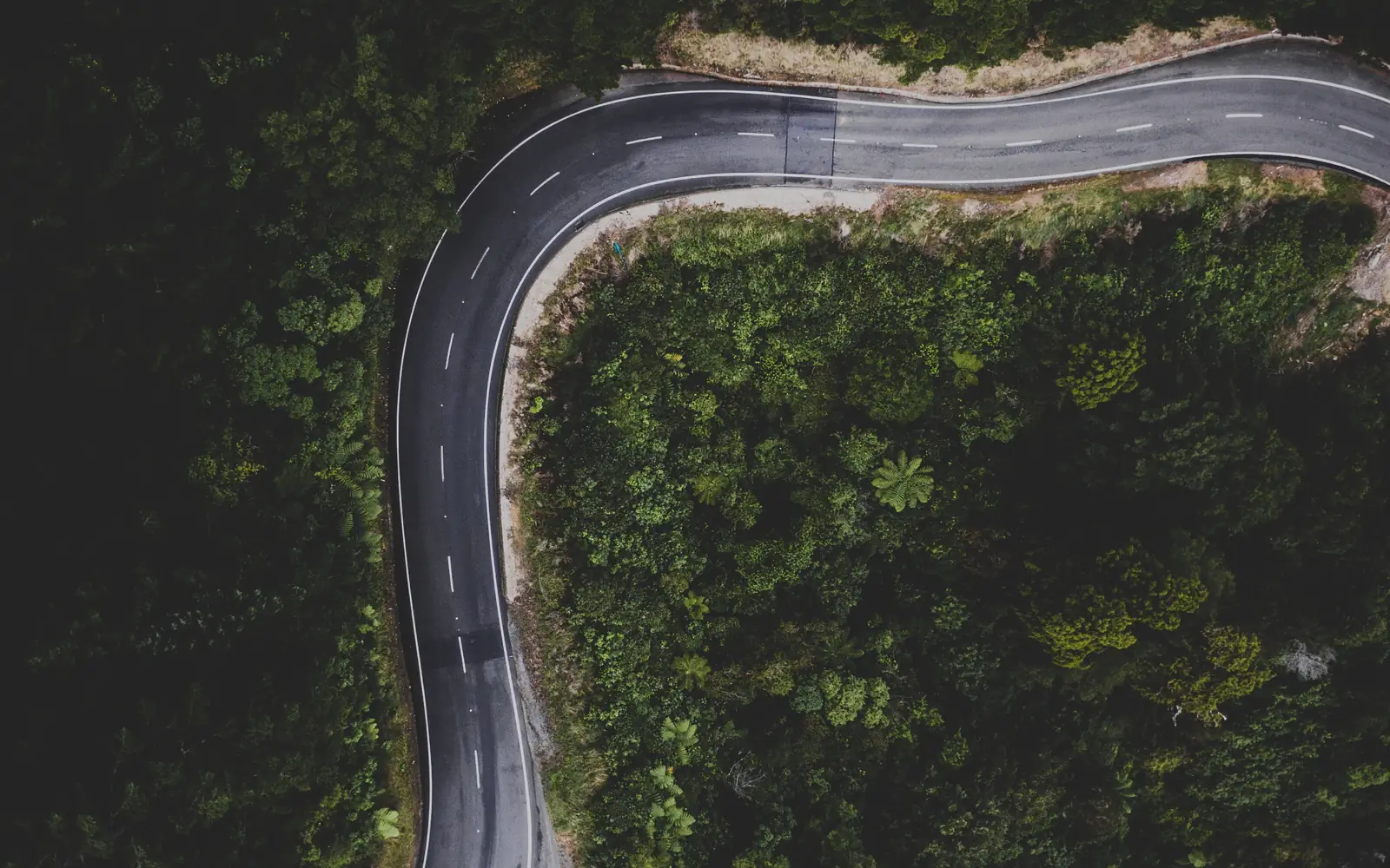An aerial view of an empty road curving through forested hills