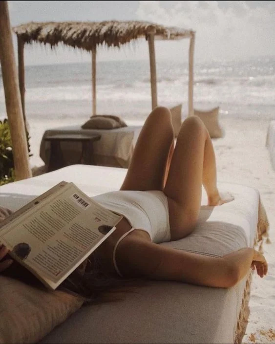 A guest reading on a shaded daybed on a quiet stretch of beach